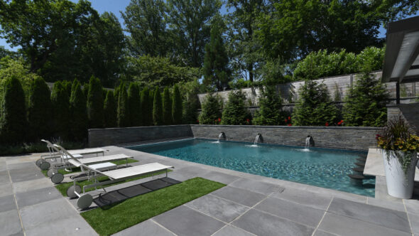 Wet-cast stone pool deck. Astro-turf, pool with water features. Bond beam wall and screening trees.