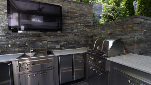 Outdoor kitchen with grill and sink, TV and hand chiseled stone wall